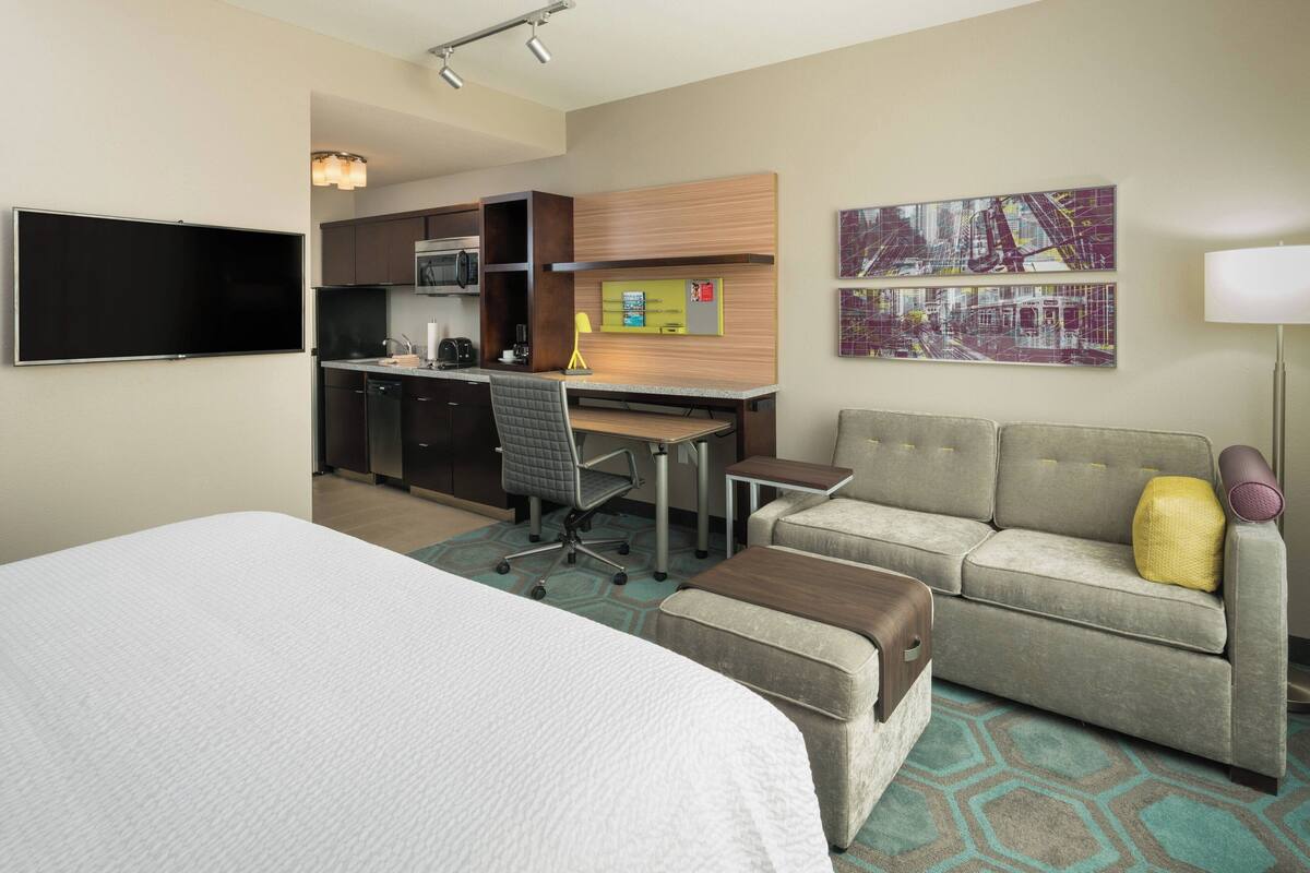 Une chambre d’hôtel comprenant un lit, un canapé, un bureau, une chaise, un téléviseur à écran plat, un four à micro-ondes, une machine à café et des œuvres d’art accrochées aux murs.