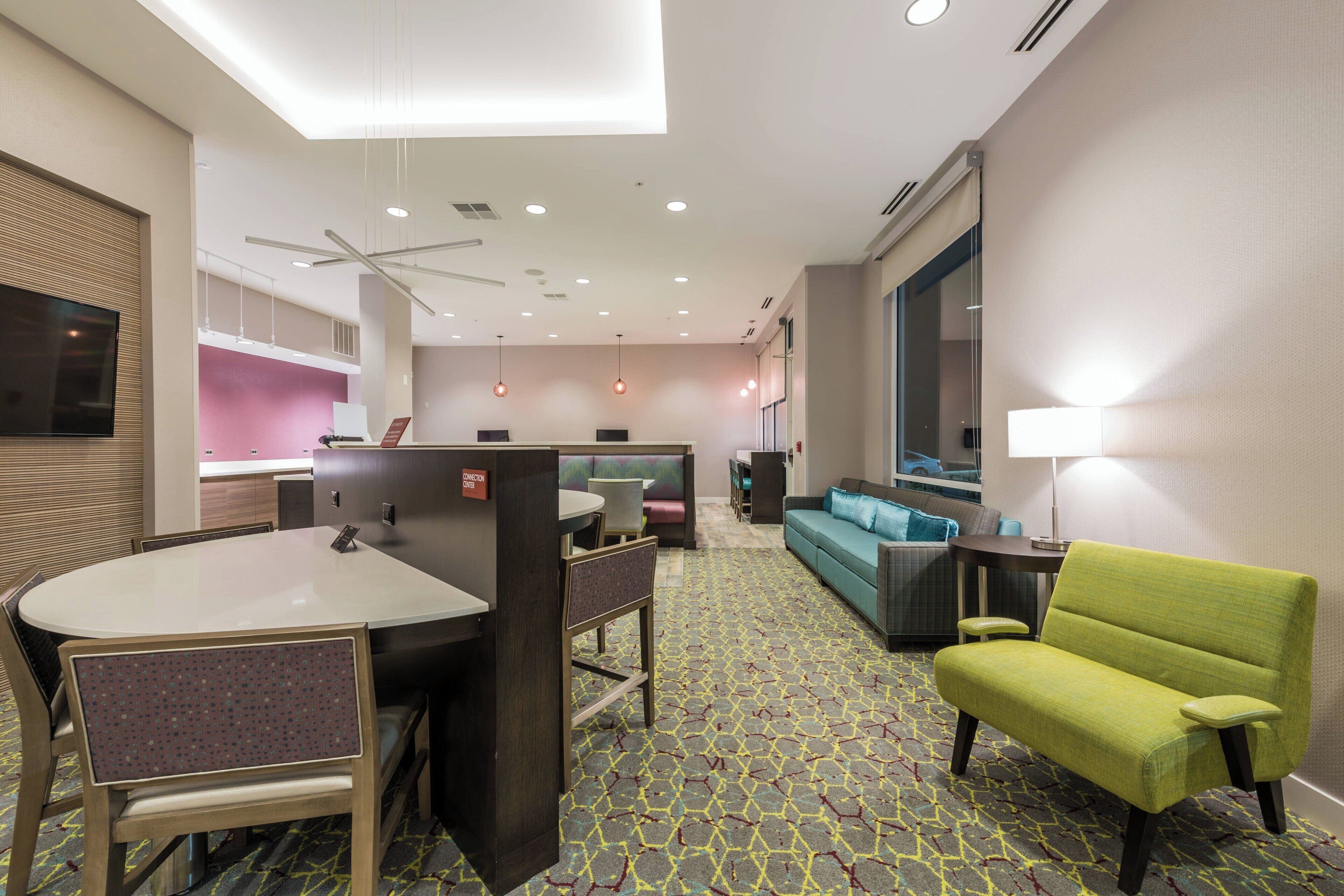 A hotel room with a dining area, a sofa, a green armchair, and a TV.