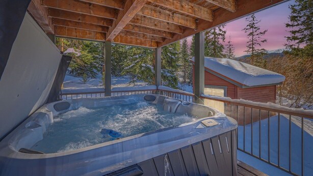 A hot tub on a wooden deck with a view of snow-covered trees and a mountain in the background.
