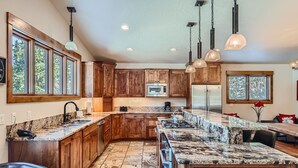 A spacious kitchen with wooden cabinets, granite countertops, and a large island. There are stainless steel appliances, including a refrigerator and a microwave.
