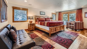 A bedroom with a wooden bed, a leather sofa, a patterned rug, and large windows with curtains.