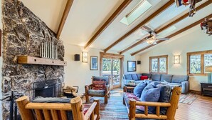 A cozy interior with a stone fireplace, wooden furniture, and large windows offering views of the outdoors.