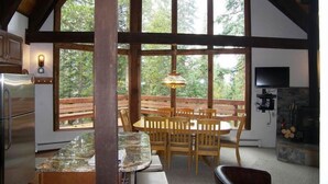 A kitchen with a wooden dining area, large windows, and a stone fireplace.