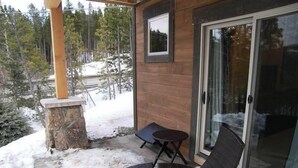 Eine überdachte Terrasse mit zwei Stühlen, einem kleinen Tisch, einem Steingartenbeet und einer Glastür, die zu einem verschneiten Außenbereich führt.