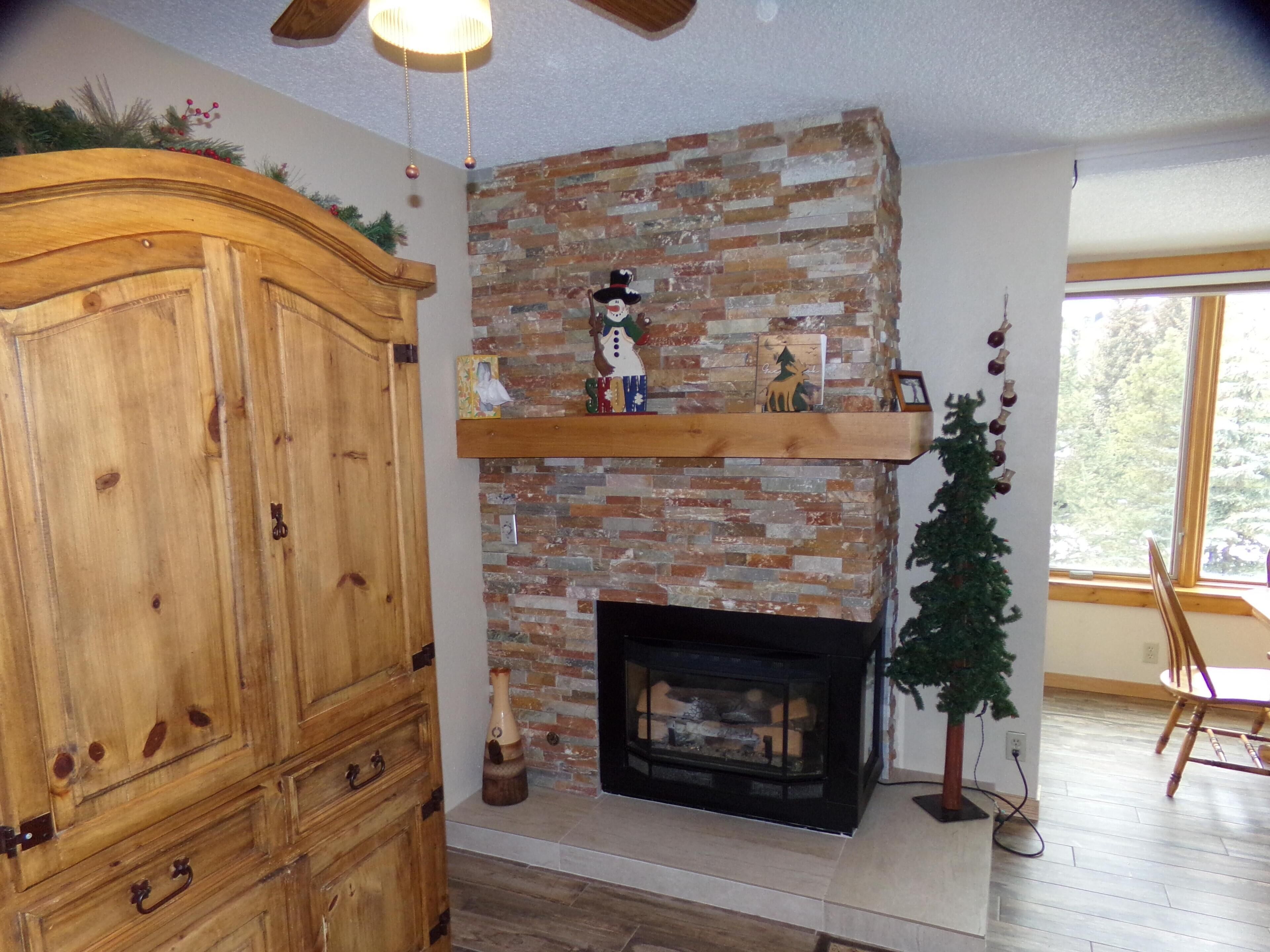 A living room with a brick fireplace, wooden cabinet, and a small Christmas tree.