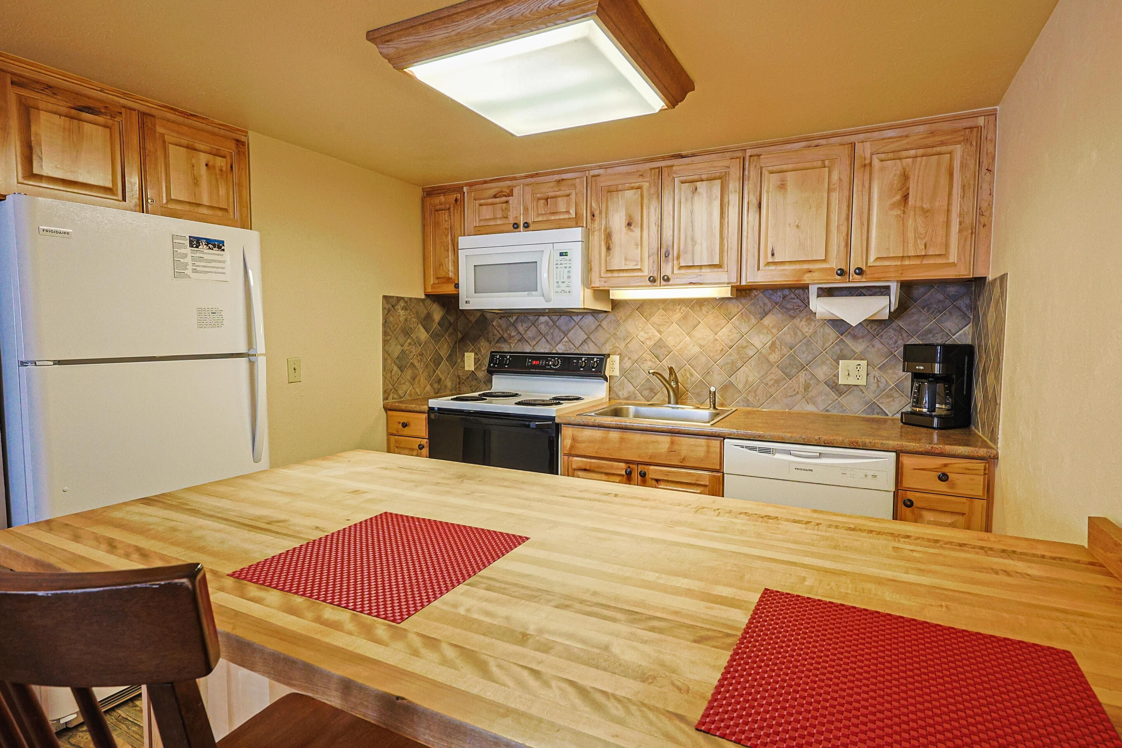 Una cocina con gabinetes de madera, refrigerador, microondas, estufa, pileta y lavavajillas.