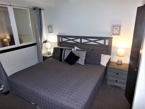 A single bed with a headboard, two bedside tables with lamps, a window with curtains, and a door. - Snowflake 1 Bed plus Den 2 Bath (Copper Mountain)