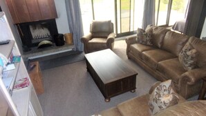 A living room with a fireplace, leather sofas, a coffee table, and a view through large windows. - Snowflake 1 Bed plus Den 2 Bath (Copper Mountain)