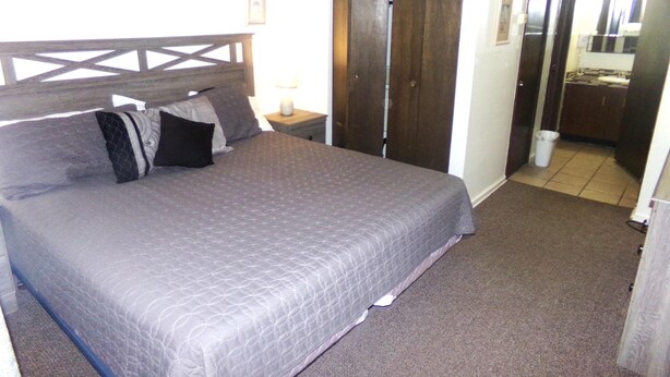 A bed with a headboard, pillows, a nightstand with a lamp, a wardrobe, and a bathroom visible in the background. - Snowflake 1 Bed plus Den 2 Bath (Copper Mountain)