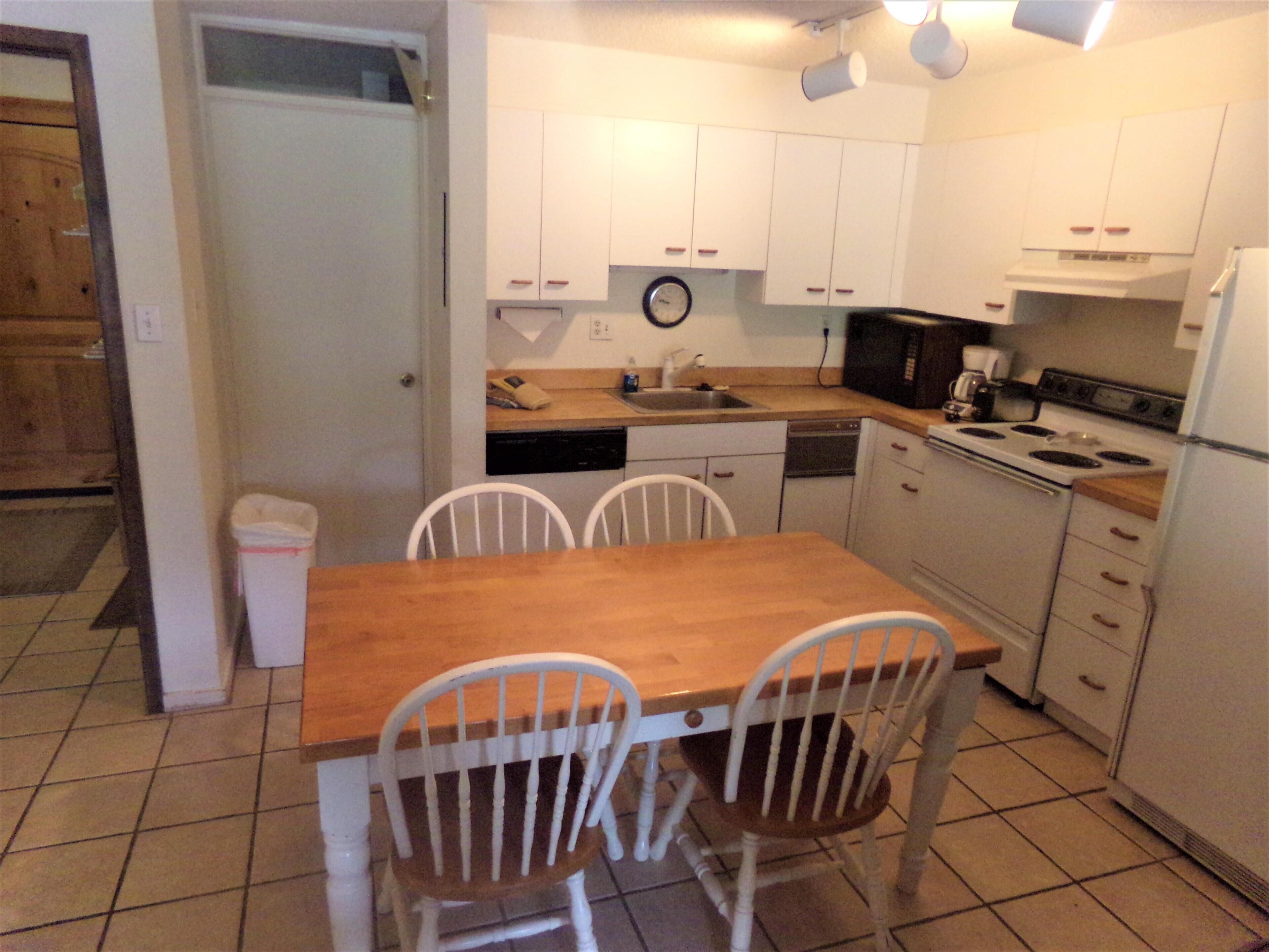 A compact kitchen with white cabinets, a wooden table, and chairs.