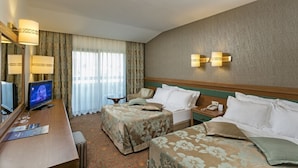 Una habitación de hotel con cama, escritorio con televisor, lámpara y ventana con cortinas.