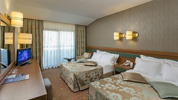 A hotel room with a bed, a desk with a TV, a lamp, and a window with curtains. - Ozkaymak Incekum Hotel (Alanya)