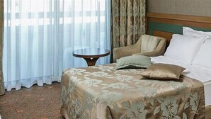 Una habitación de hotel con cama, una silla, una mesita y cortinas.