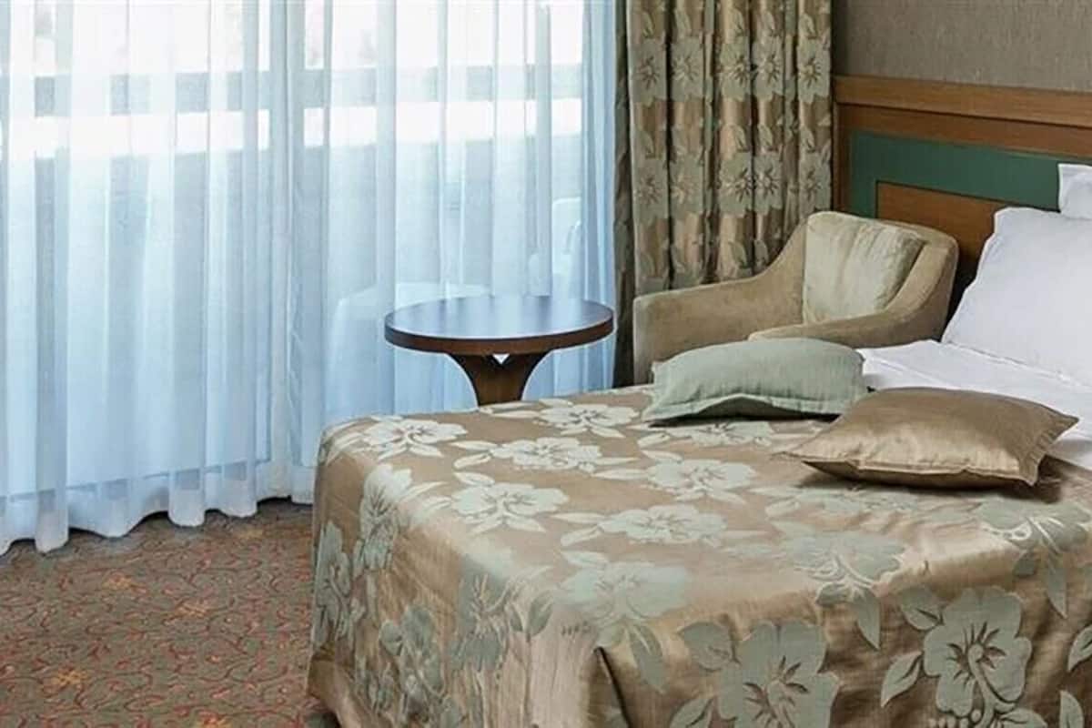 Hotellihuone, jossa on sänky, tuoli, pieni pöytä ja verhot.