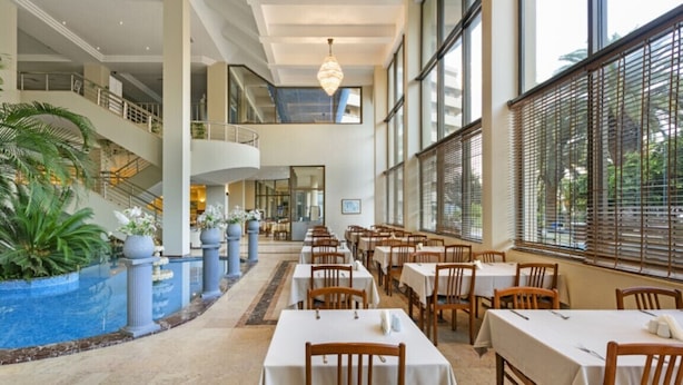 Un vestíbulo de hotel con piscina, varias zonas de comedor y una escalera que lleva a un nivel superior.