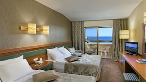 Habitación de hotel con dos camas, televisión, escritorio con computadora, teléfono y balcón con vista al mar.