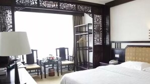 A hotel room with a bed, a desk with a lamp, a chair, a small table, and a wardrobe. - Li River (Guilin)