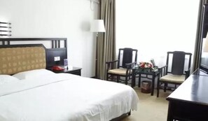 Habitació d'hotel amb un llit gran, un escriptori amb una cadira, una taula petita amb una cadira i una finestra amb cortines.