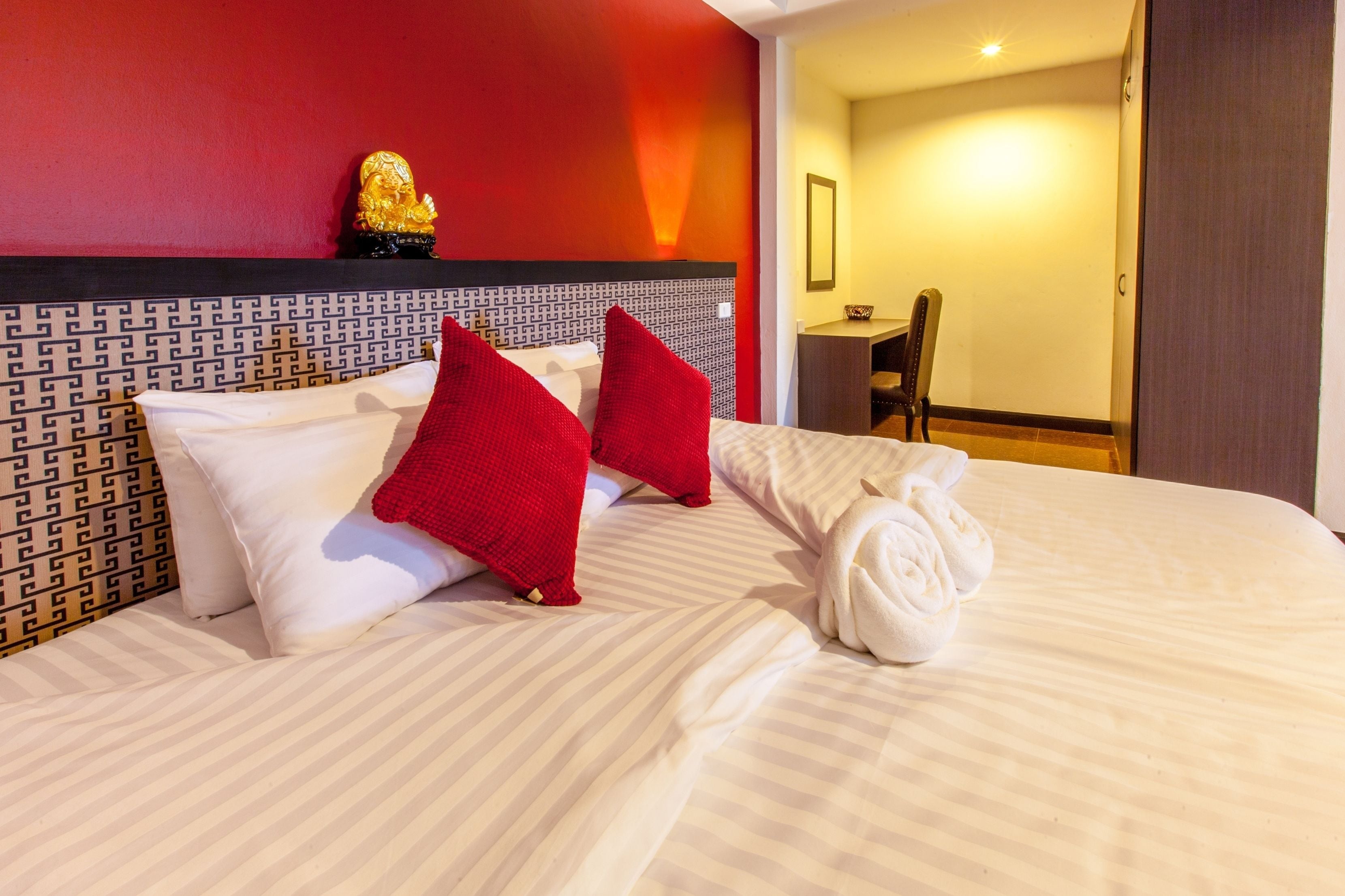 A hotel room with a bed, red pillows, a golden statue, and a chair.