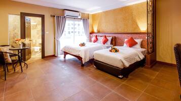 Habitación de hotel con dos camas, una sala de estar con una mesa y sillas, y vistas de la ciudad a través de la ventana.