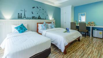 A hotel room with two beds, a desk, a chair, and a wall with a cityscape mural.