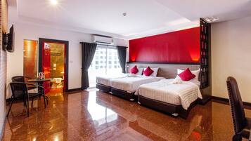 A hotel room with two beds, a sitting area with a chair and table, a red accent wall, and a view of the city through the window.