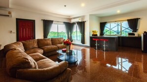 A modern living room with a brown leather sofa, a glass coffee table with a vase of flowers, and a kitchen area with a microwave and a red countertop. - Gallery Lake View Hotel (Khon Kaen)