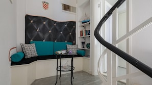 A corner seating area with a tufted headboard sofa, a small table, and a chair. - PLR Accommodation (Split)