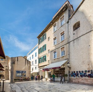A historic street with buildings featuring traditional architecture, a cobblestone street, and a shop with a red awning. - PLR Accommodation (Split)
