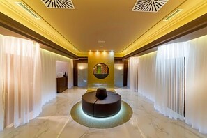 A hotel lobby with a central circular seating area, a reception desk, and a decorative wall with a circular design.