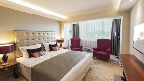 A hotel room with a large bed, two armchairs, a small table, and a desk.