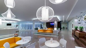 A modern hotel lobby with a reception desk, seating area, and decorative lighting.