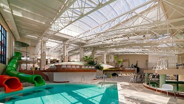 An indoor swimming pool with a glass ceiling, slides, and sunlit terraces.