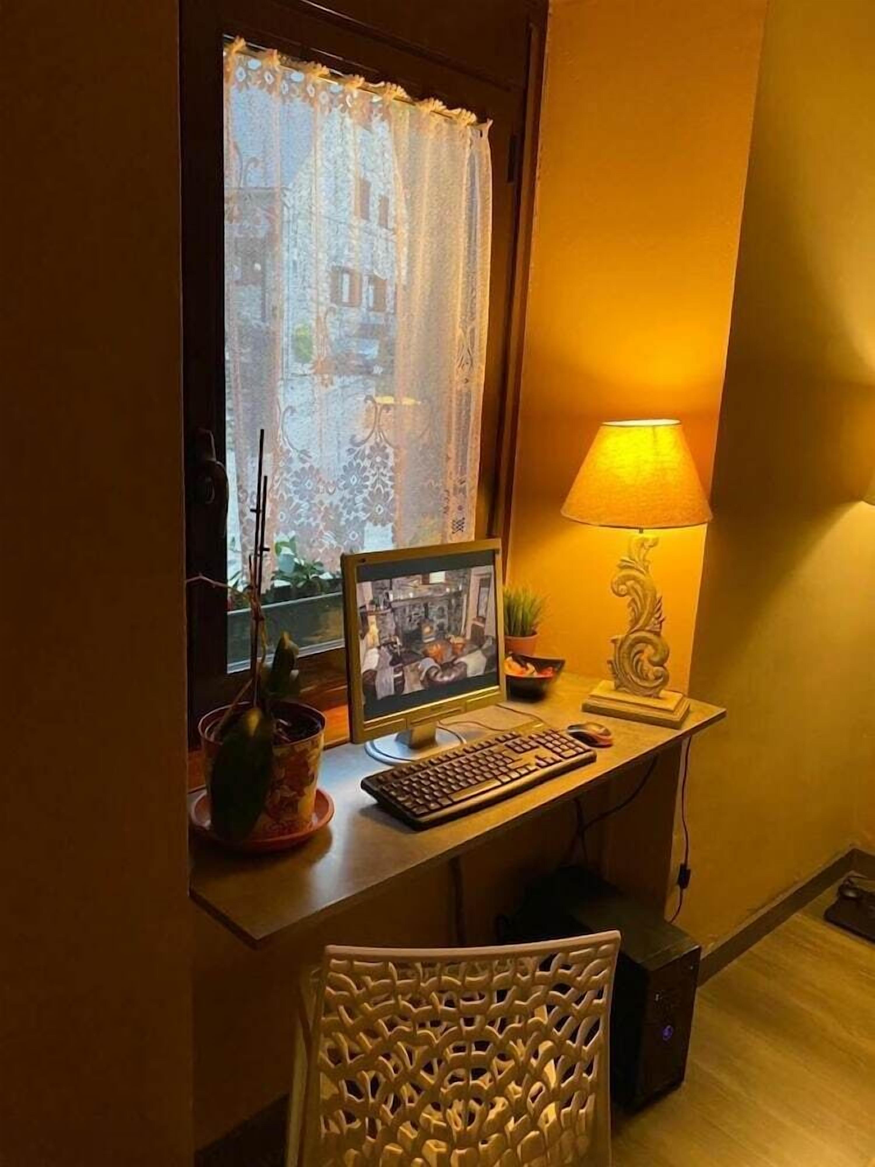 A desk with a computer, a lamp, and a window with a curtain.