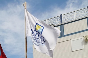 A flag with the text "HOTEL RESTAURANTE DEIRANTES" and a logo, mounted on a flagpole. - Hotel Bandeirantes (Balneario Barra do Sul)