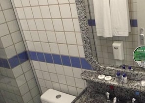 A bathroom with a tiled wall, a toilet, a sink with a mirror, and a soap dispenser. - Hotel Bandeirantes (Balneario Barra do Sul)