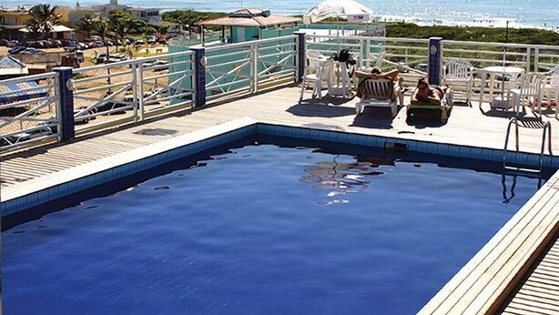 A swimming pool with lounge chairs and umbrellas, overlooking a beach and the sea. - Hotel Bandeirantes (Balneario Barra do Sul)