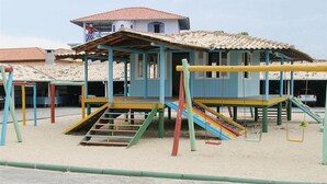 A playground with colorful equipment and a building in the background. - Hotel Bandeirantes (Balneario Barra do Sul)