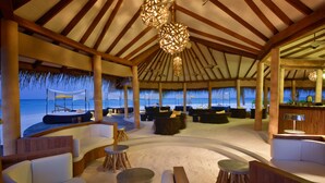 Un espace de détente intérieur doté d’un toit de chaume, de meubles en bois et offrant une vue sur la plage.