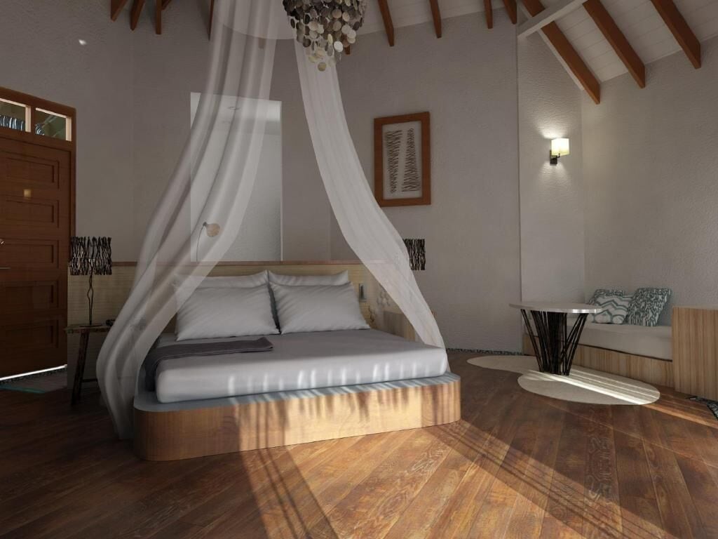 Un dormitorio con una cama bajo dosel, una mesita de noche, una lámpara de pared y una pequeña zona de estar con cojines.