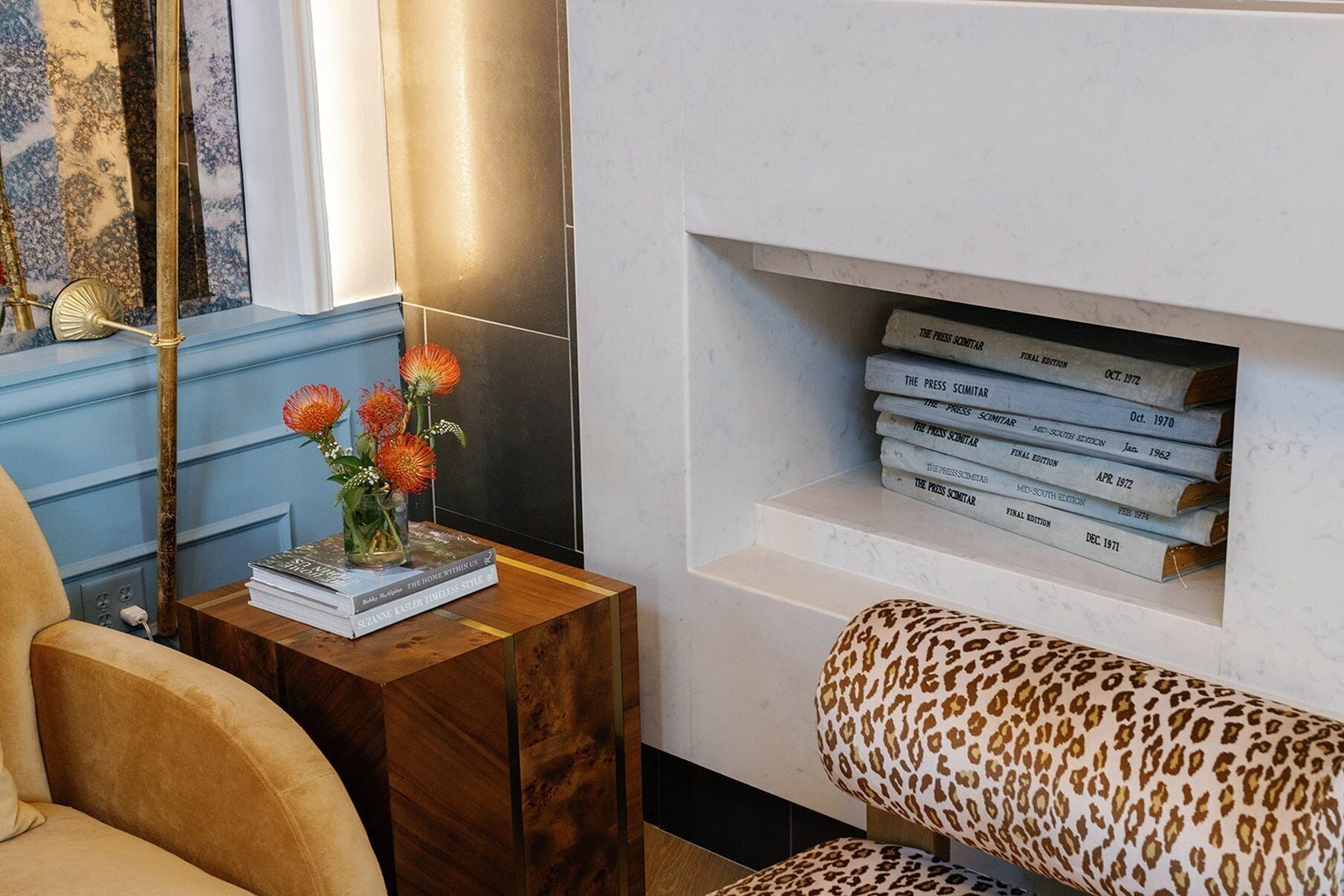 A living room with a bookshelf, a small table with a vase of flowers, and a leopard print sofa.