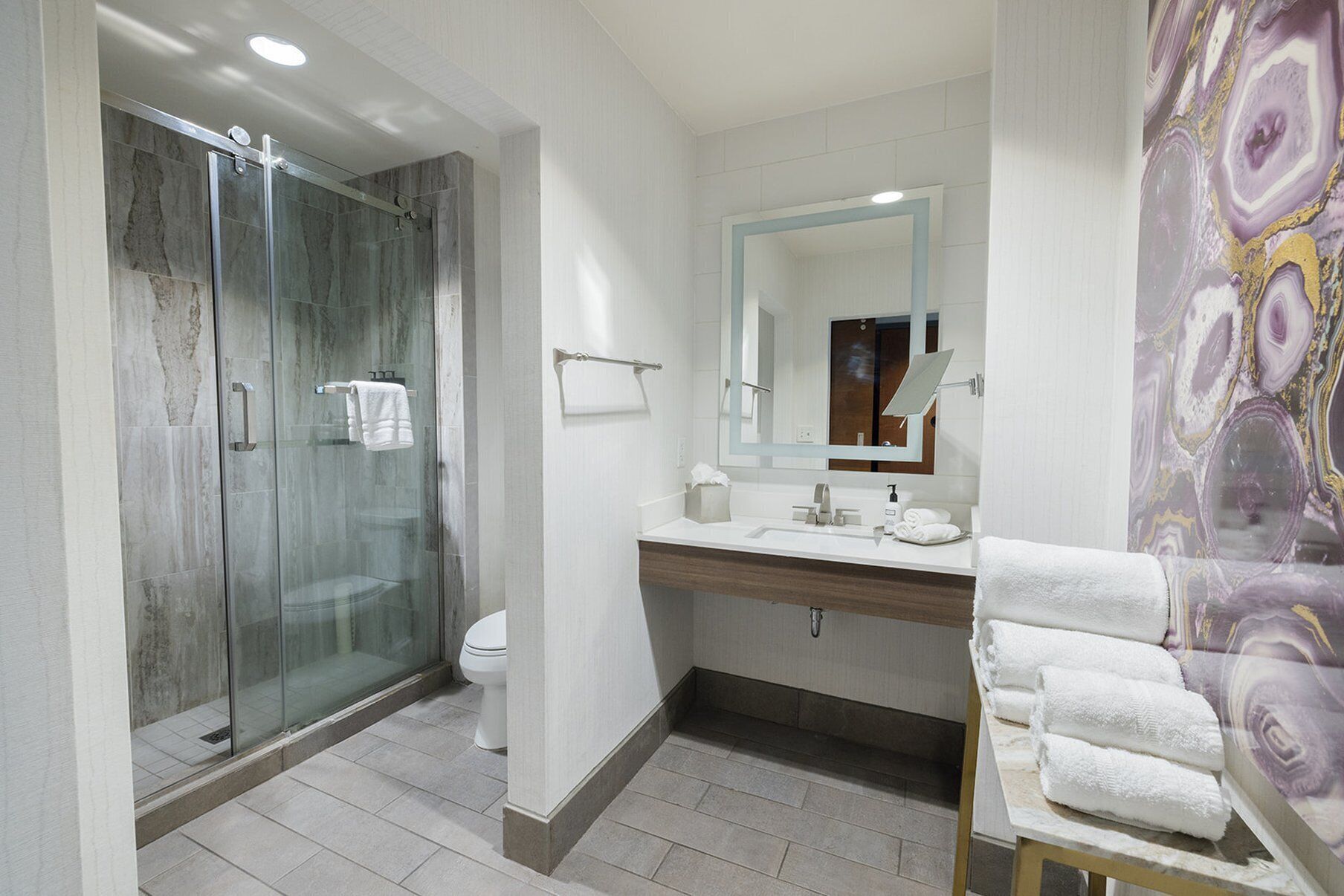 A modern bathroom with a glass-enclosed shower, a white toilet, a vanity with a mirror, and a towel rack.