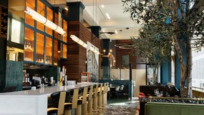 Un bar moderno con una barra alargada, varios taburetes y una zona de estar con un sofá verde.