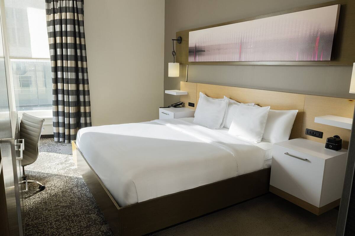 A hotel room with a large bed, bedside tables, a desk, and a chair.
