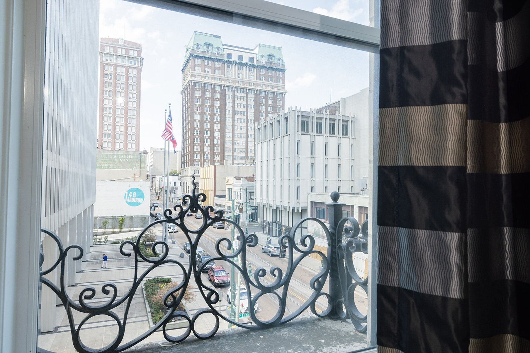 A view from a window with ornate black iron railings, a street with cars, and buildings in the background.