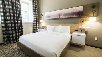 A hotel room with a large bed, a nightstand, a lamp, and a painting on the wall.