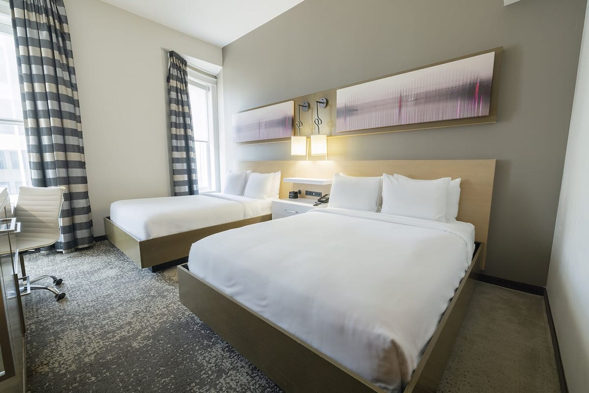 A hotel room with two single beds, a desk, a chair, and a large window with curtains.