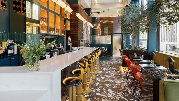 Zona de bar moderna con una barra alargada, varios taburetes y un área de estar con mesas y sillas.