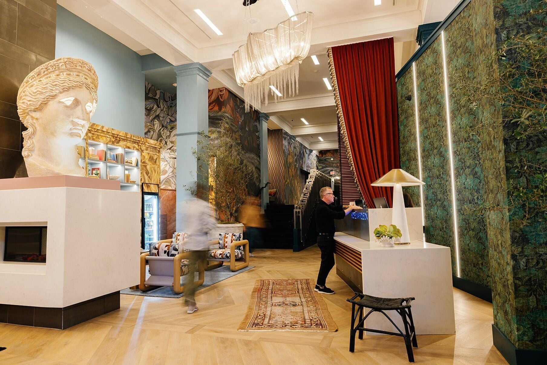 A modern lobby with a large bust sculpture, a reception desk, and a staircase.