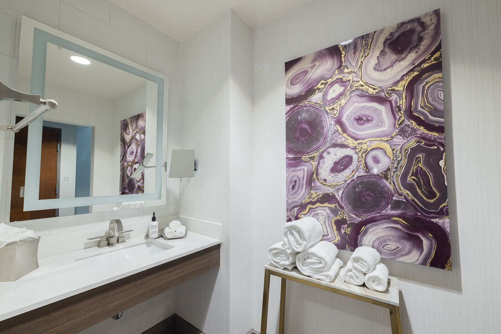 Een moderne badkamer met een wit wastafelmeubel, een grote spiegel en wanddecoratie met een marmerprint.